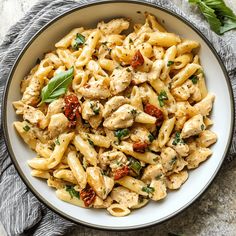 a white bowl filled with pasta covered in chicken and sauce on top of a gray towel