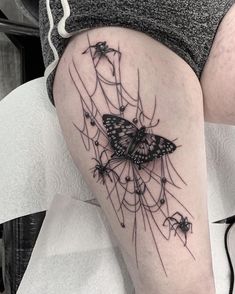 a woman's thigh with a butterfly tattoo on her leg and spider webs