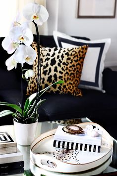 a living room with black couches and white orchids in a vase on the coffee table