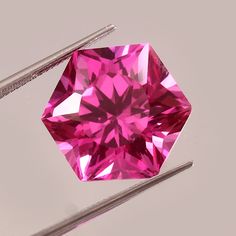 a pink diamond sitting on top of two needles next to another piece of metal material