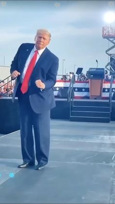 a man in a suit and red tie standing on stage with an american flag behind him