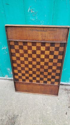 a wooden chess board sitting on top of a cement floor next to a blue wall