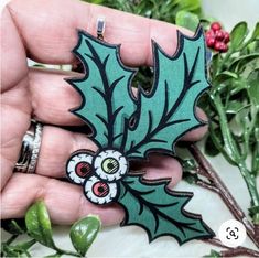 a hand holding a green and black holly brooch