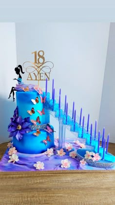 a three tiered blue cake with purple flowers and candles on the bottom is displayed