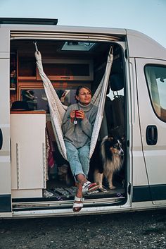 a woman sitting in the back of a van with her dog