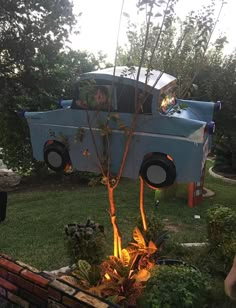 a blue truck parked in the grass next to a tree and fire pit with people looking at it