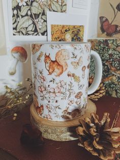 a coffee cup sitting on top of a wooden table next to pine cones and pictures