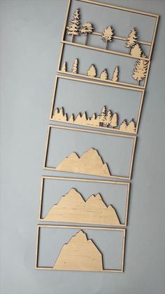 three wooden cutouts with trees and mountains on them, one is in the shape of a ladder