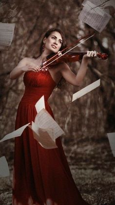 a woman in a long red dress holding a violin and papers flying from her hands