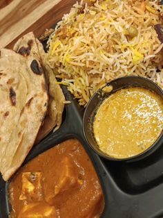 a black plate topped with rice, naan and sauces next to other foods