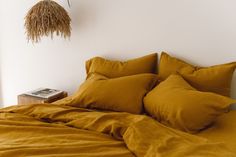 a bed with yellow sheets and pillows in a white room next to a plant hanging on the wall