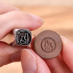 a person holding a wooden ring with a potter's pottery logo on it and another item in the background