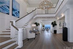 a large foyer with white walls and wood flooring, chandelier above the staircase