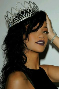 a woman wearing a tiara and holding her hair in one hand while standing against a wall