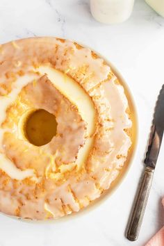 a bundt cake with icing on a plate next to a knife and fork