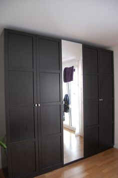 an empty room with large black cabinets and wood flooring on the side, in front of a window