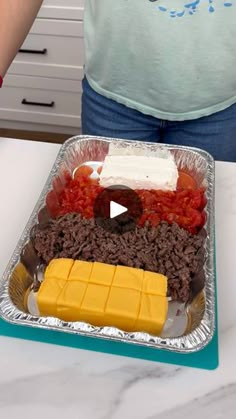 a person standing in front of a tray of food on a kitchen counter with cheese, meat and vegetables