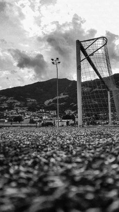 a black and white photo of a soccer goal in the middle of a field with mountains in the background