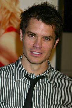 a man wearing a striped shirt and black tie posing for a photo in front of a poster