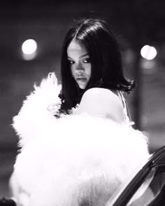 a black and white photo of a woman in fur coat standing next to a car