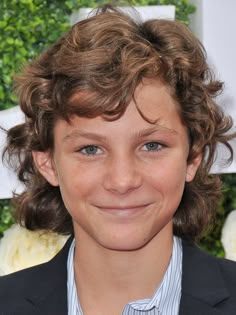 a close up of a person wearing a suit and tie with curly hair smiling at the camera