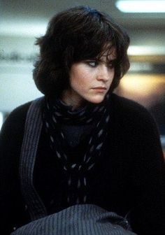 a woman with short hair wearing a scarf and black sweater looking off to the side