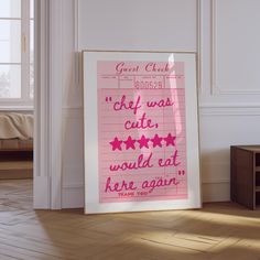 a pink poster with writing on it sitting in front of a white wall and wooden floor