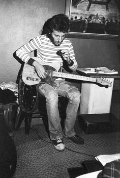 black and white photograph of a man playing guitar in a room with other items on the floor