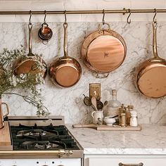 pots and pans are hanging on the wall above an oven in a kitchen with marble counter tops