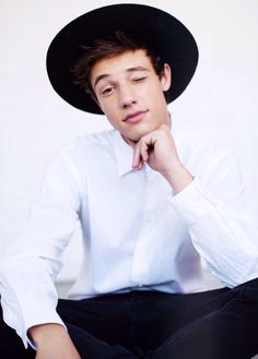 a young man wearing a black hat and sitting on the floor with his hand under his chin