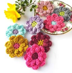 four crocheted flowers sitting on top of a plate next to a flower plant