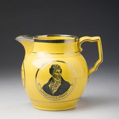 a yellow pitcher with a drawing of a man on the front and side, sitting against a gray background