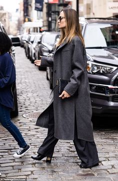 a woman is walking down the street with her hand in her pocket and wearing sunglasses