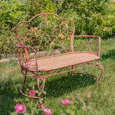 an iron bench sitting in the grass near some pink flowers and trees with green leaves