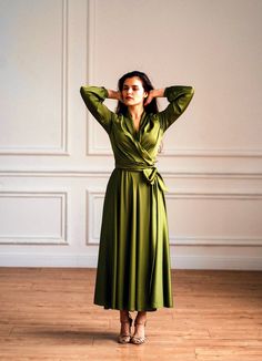 a woman in a green dress standing on a wooden floor with her hands behind her head