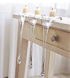 three candles are placed on the side of a wooden table with clear glass holders holding them