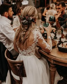 the back of a bride's dress sitting at a table with candles in front of her