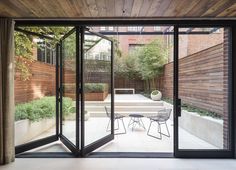 an open glass door leading to a patio with chairs and table in the middle of it