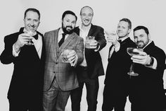 four men in suits are holding wine glasses and posing for a black and white photo