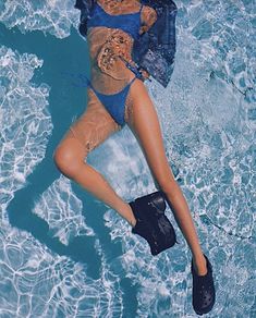 a woman laying in the water wearing a blue swimsuit and black shoes with her legs spread out