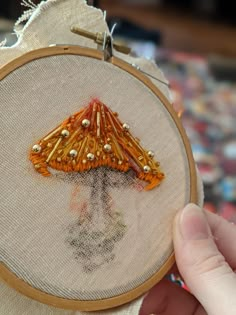 a close up of a person's hand holding a small cross stitched object