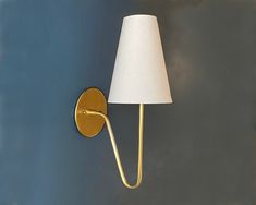 a gold wall light with a white shade on it's side and a blue background