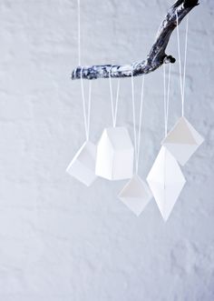 an origami mobile hanging from a tree branch in front of a white wall