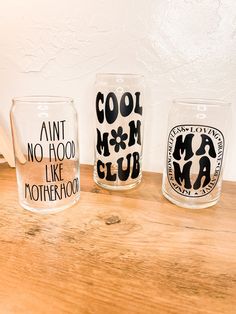 three glasses sitting on top of a wooden table next to each other with words painted on them