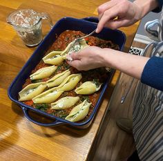 a woman is spooning some food out of a blue casserole dish on a wooden table