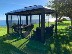 a gazebo sitting on top of a lush green field next to the ocean and trees