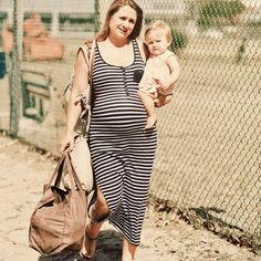 a woman holding a baby in her arms while walking down the street with a handbag