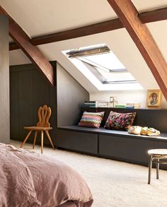 a bed sitting under a skylight in a bedroom next to a wooden desk and chair