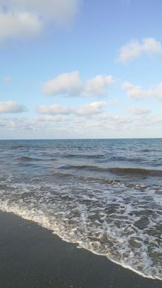 the ocean waves roll in and out onto the beach with white clouds above it on a sunny day