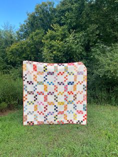 a colorful quilt on the grass in front of some trees